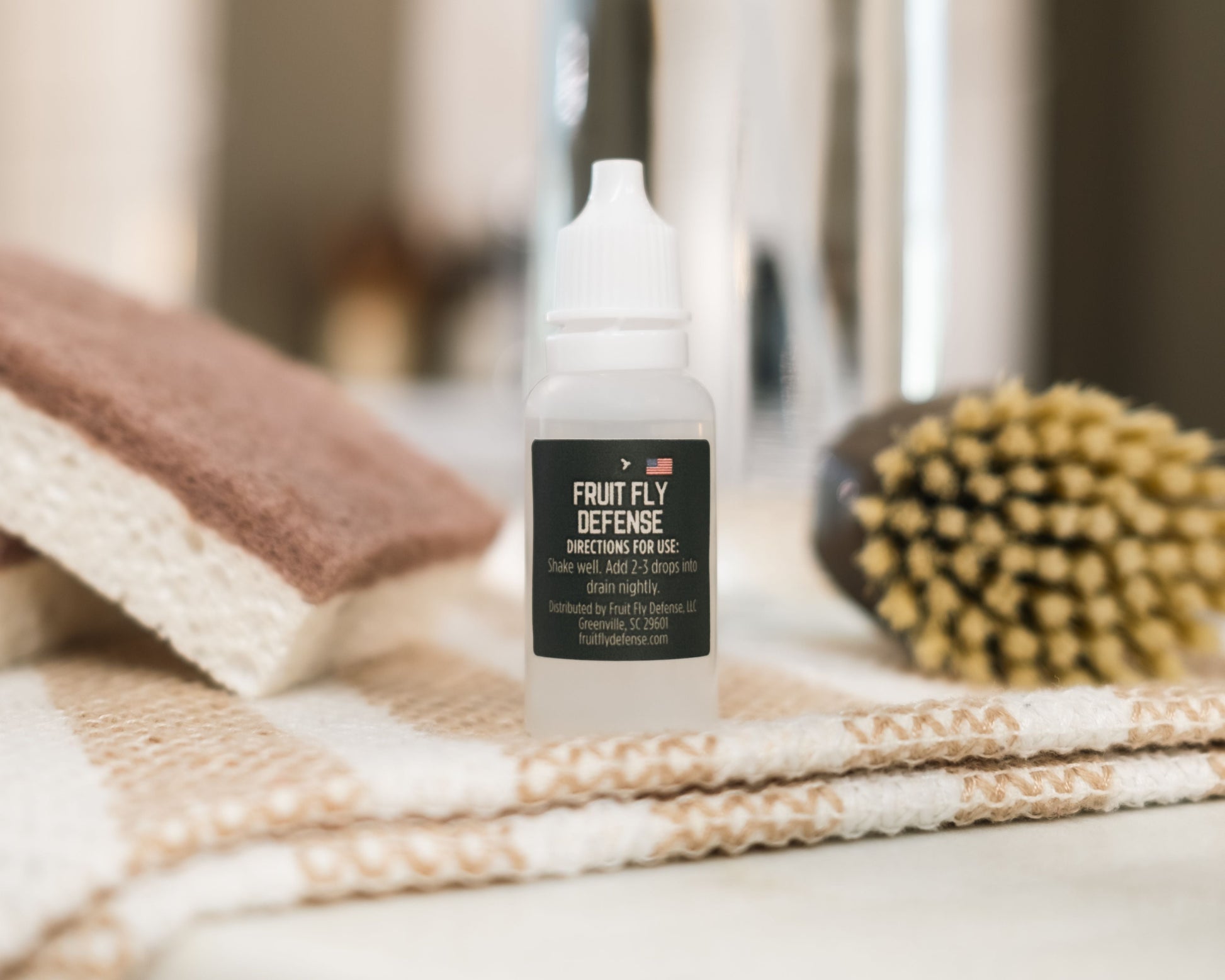 Small bottle labeled 'Fruit Fly Defense' on a surface with cleaning tools in the background