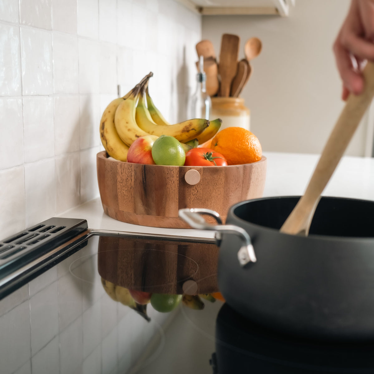 Kitchen scene with a pot on the stove, wooden bowl of fruit, and person stirring. Fruit Fly Defense disc in the back by a bowl of fruit.