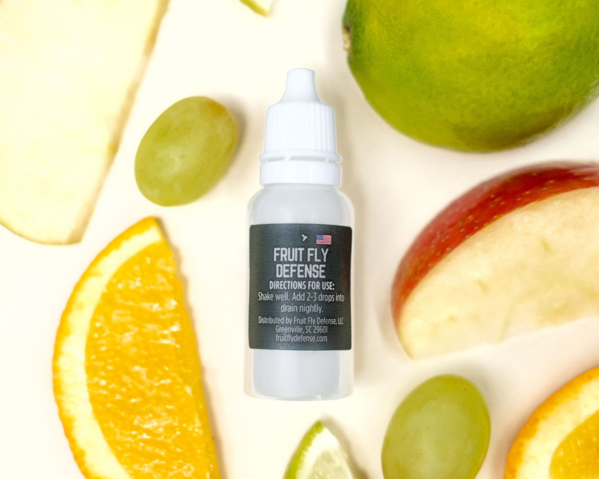 Fruit Fly Defense Sink Drops bottle surrounded by fresh kitchen fruit — plant-based drain treatment